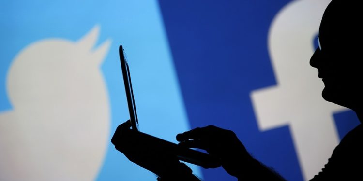 A man is silhouetted against a video screen with a Twitter and a Facebook logo as he poses with an Dell laptop in this photo illustration taken in the central Bosnian town of Zenica, August 14, 2013. REUTERS/Dado Ruvic (BOSNIA AND HERZEGOVINA - Tags: BUSINESS TELECOMS) - RTX12L7W